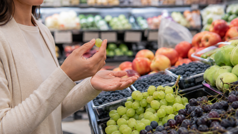 Kundin hält eine Weintraube in der Obstabteilung eines Supermarkts [Bildinhalt mit KI erstellt]